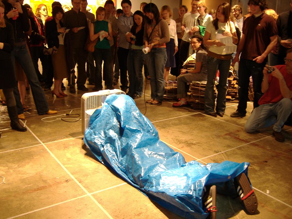photo of me laying down in front of a box fan in an art gallery with a tarp attached to my body
