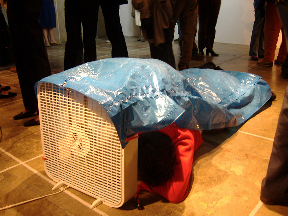 close-up photo of me laying down in front of a box fan in an art gallery with a tarp attached to my body
