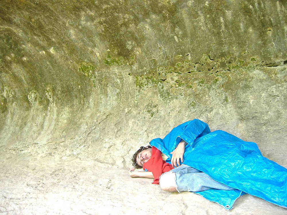 photo of me lying down, wrapped up in a tarp, against a rock wall