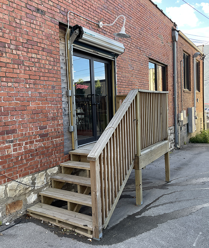 Photo of a wooden staircase leading to a glass door in a brick alley. The door says 100 million in loopy red numbers.